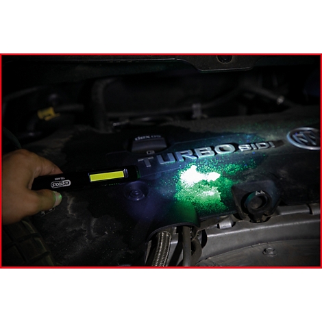 Een hand houdt een werkplaatslamp boven een motor. De motor gloeit groen in het licht, de tekst "TURBO SIDI" is te zien.